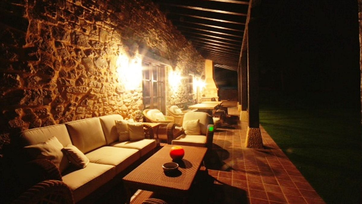 Porche del caserío de noche, con sofás y luz cálida de lámparas