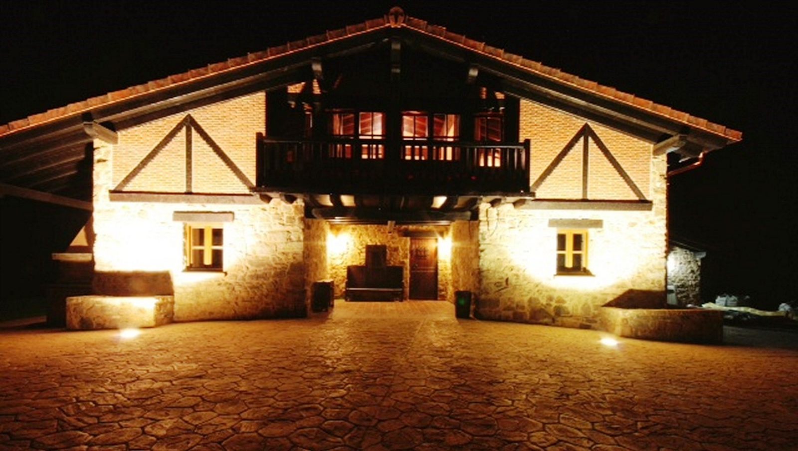 El caserío Butrón iluminado de noche, fachada de piedra y entramado de madera